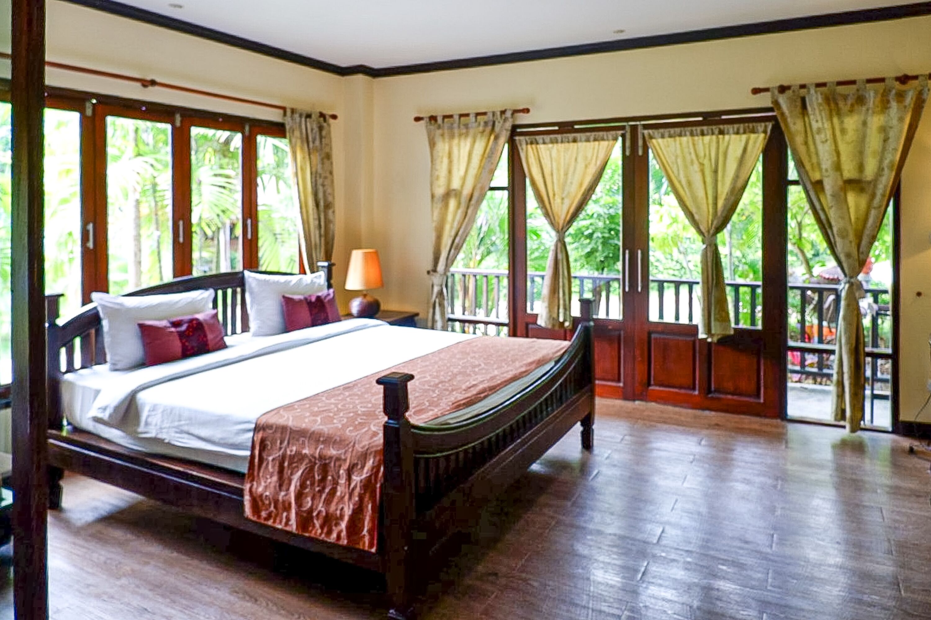 A bedroom with a wooden bed, curtains, and a view of greenery outside.