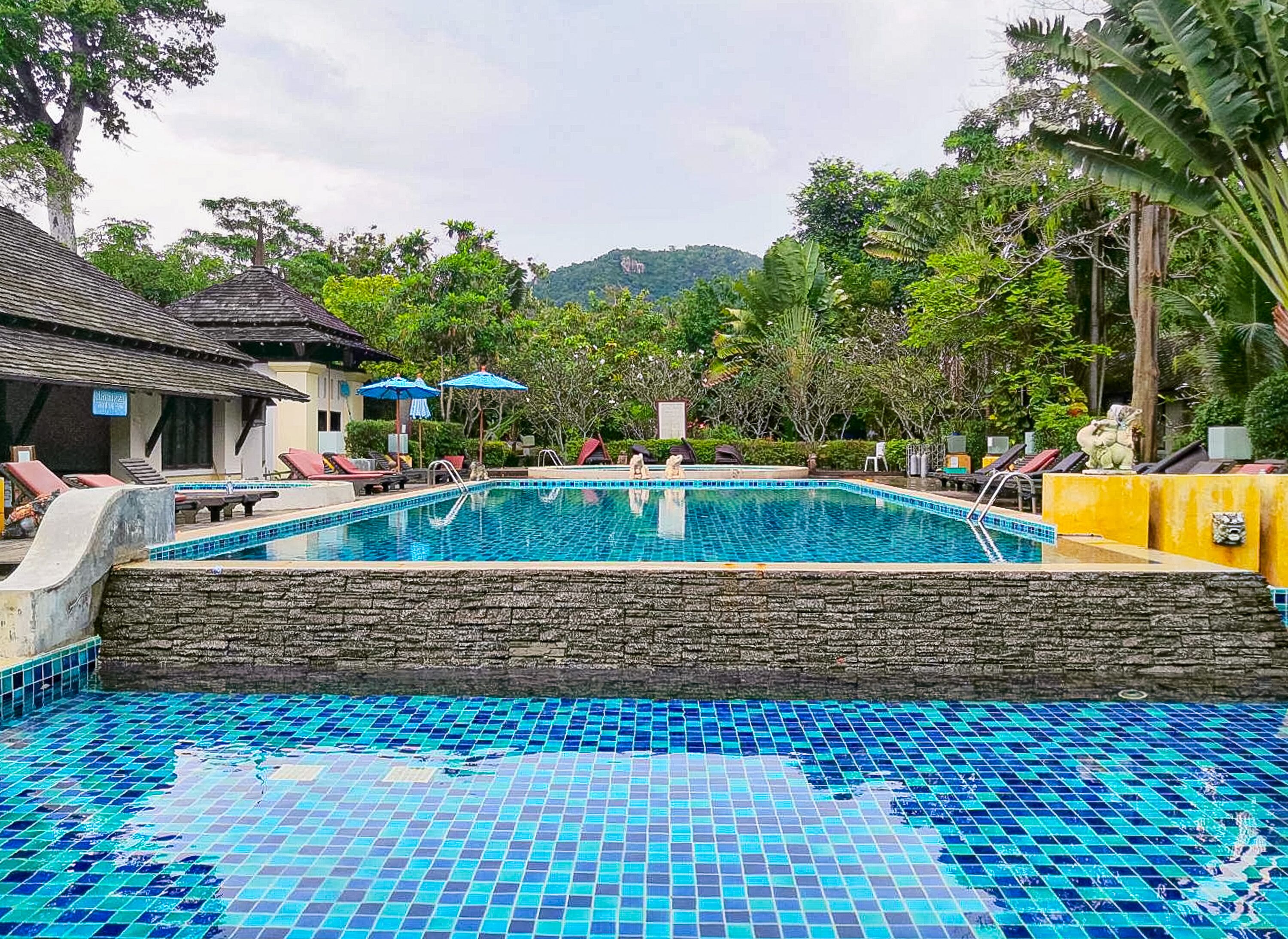 A swimming pool with tiled blue floor and walls, surrounded by lounge chairs and umbrellas.