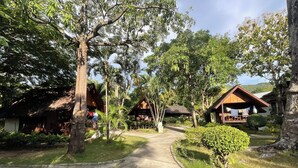 A rustic wooden cabin with a thatched roof, surrounded by lush greenery and palm trees. - Seashell Resort Koh Tao (Koh Tao)