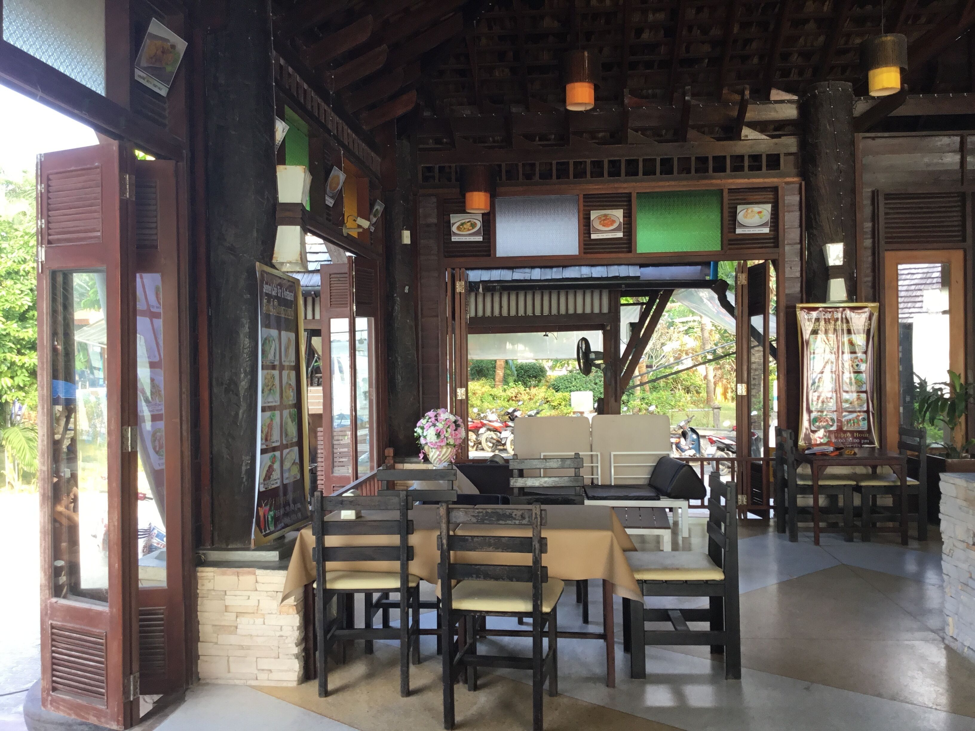Un restaurant au décor rustique, avec des poutres en bois et un mur en pierre. On y trouve des tables et des chaises disposées pour les repas, ainsi qu’un arrangement floral sur la table.