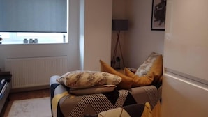 Een woonkamer met een bank, een radiator, een raam met jaloezieën en een vloerlamp.