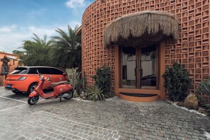 A building with a unique lattice facade, a thatched roof entrance, and a parked scooter. - Cyrus Villa Seminyak by Ini Vie Hospitality (Seminyak)