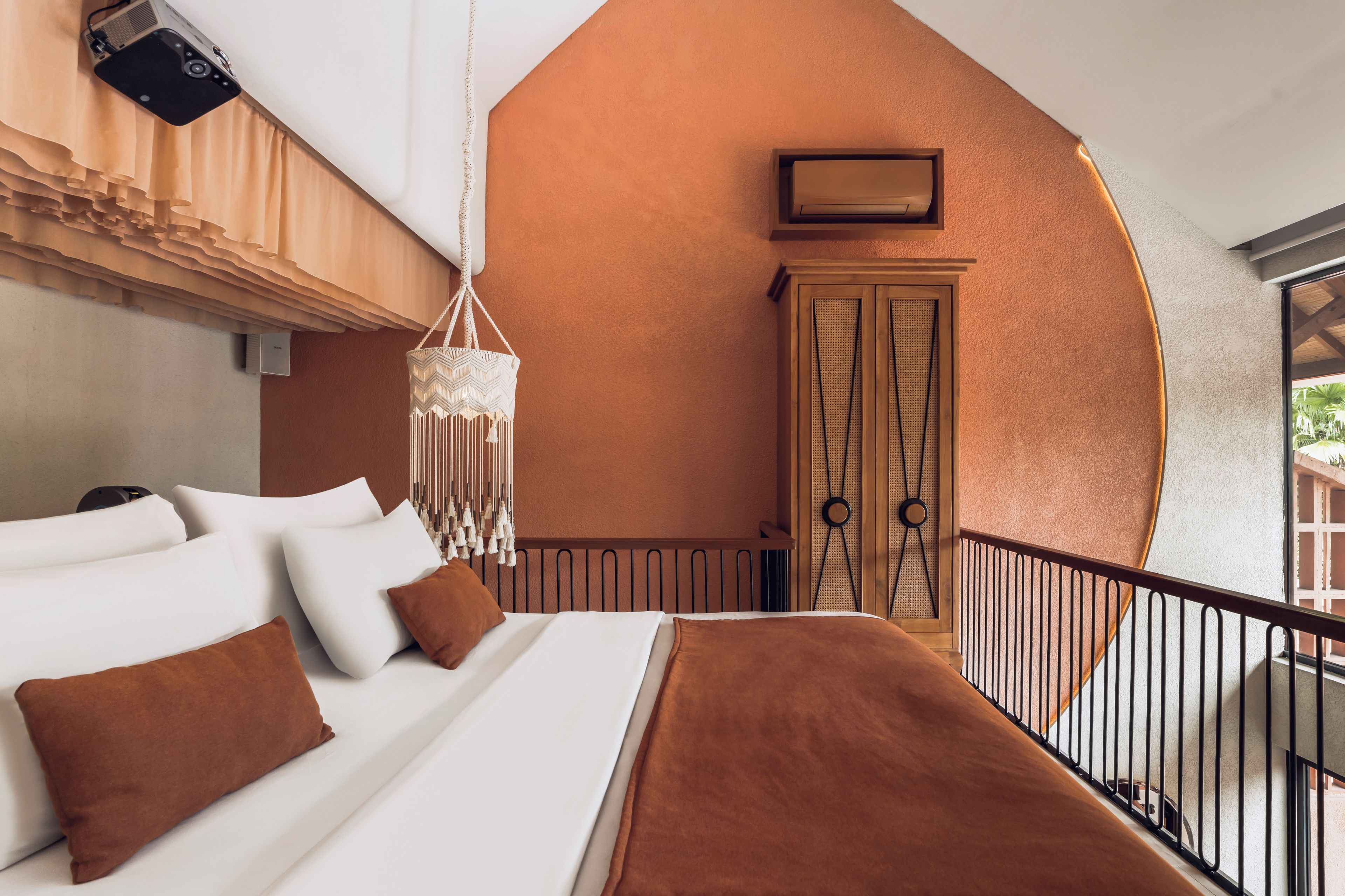 A hotel room with a bed, a hanging macrame light fixture, a wardrobe, and a balcony.