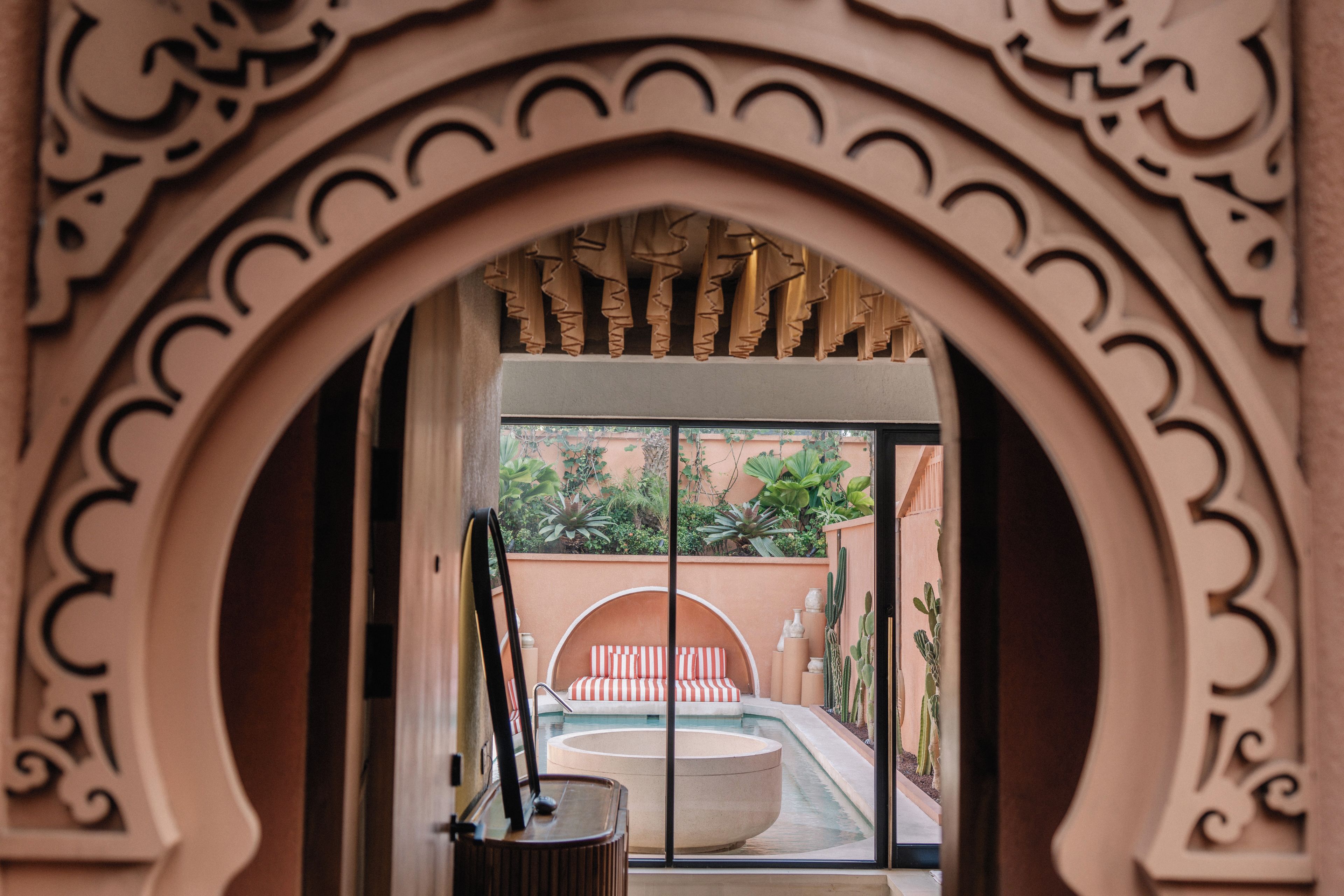 Un arco decorativo que da paso a una zona de piscina con vistas a un jardín y un edificio al fondo.