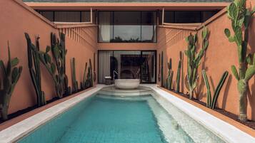 Una piscina con superficie d'acqua cristallina e blu, circondata da pareti con cactus e un edificio moderno con ampie finestre.