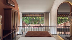 Una camera da letto con un letto grande, vista su un balcone con ringhiera in legno e una finestra che si affaccia sul verde.