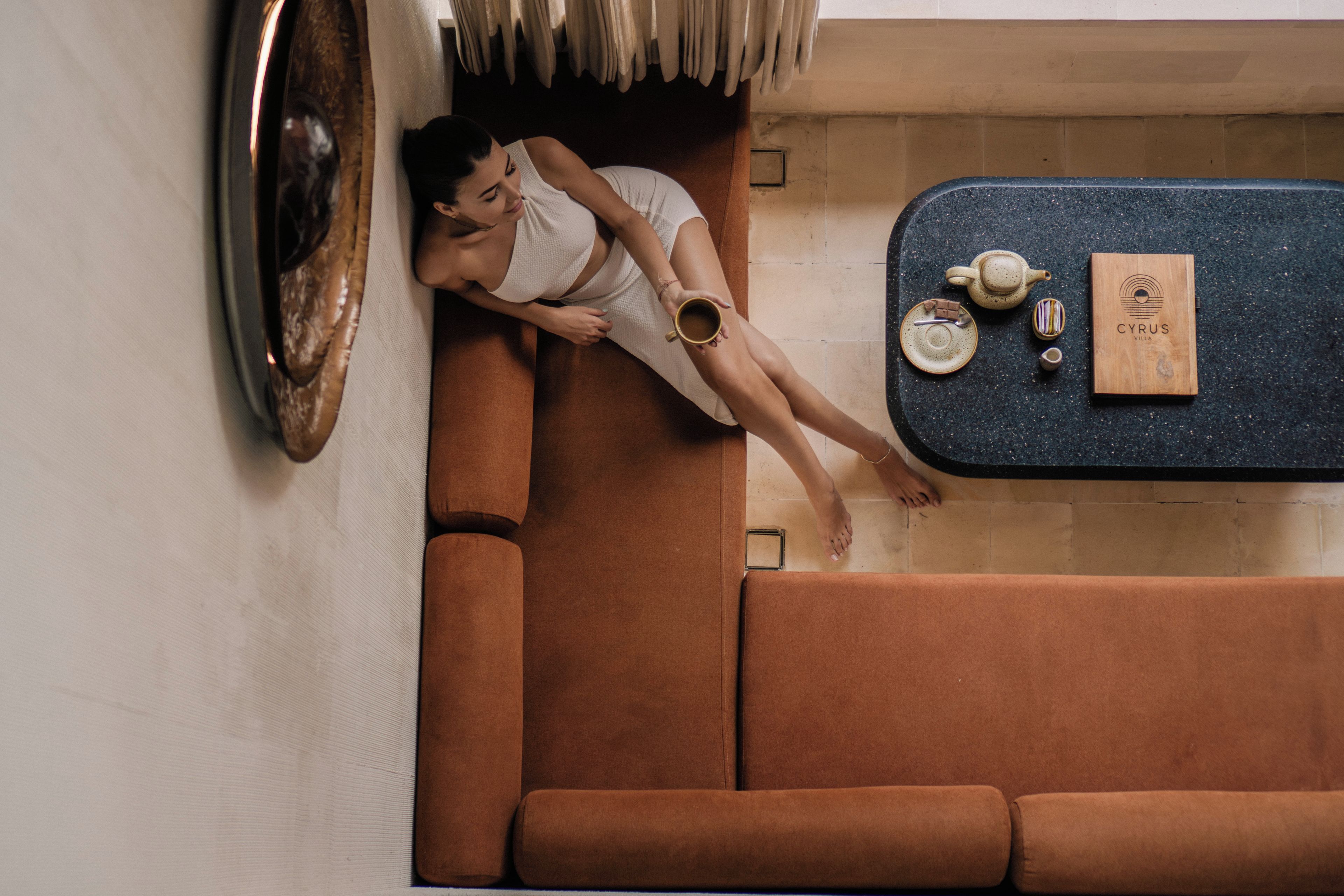 A person lying on a brown sofa in a room with a dark blue countertop, a small table, and a framed picture on the wall.