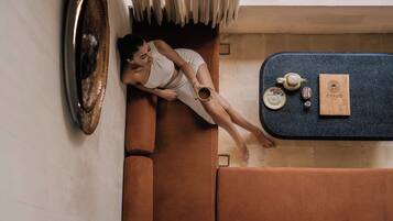 A person lying on a brown sofa in a room with a dark blue countertop, a small table, and a framed picture on the wall.
