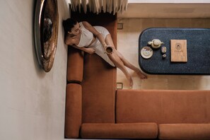 A person lying on a brown sofa in a room with a dark blue countertop, a small table, and a framed picture on the wall. - Cyrus Villa Seminyak by Ini Vie Hospitality (Seminyak)
