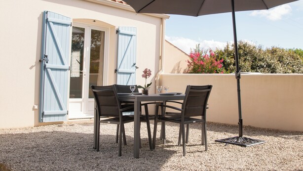Eine Terrasse im Freien mit Tisch und Stühlen, einem großen Sonnenschirm und einer Tür mit blauen Fensterläden.