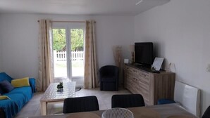 Ein Zimmer mit Esstisch, Stühlen, einer Couch, einem Fernseher und einem Schrank.