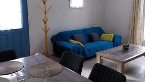 Ein Wohnzimmer mit blauem Sofa, einem Holz-Knopfleiste, einem Esstisch mit gewebten Tischsets und einem kleinen Topf mit Pflanze auf dem Tisch.