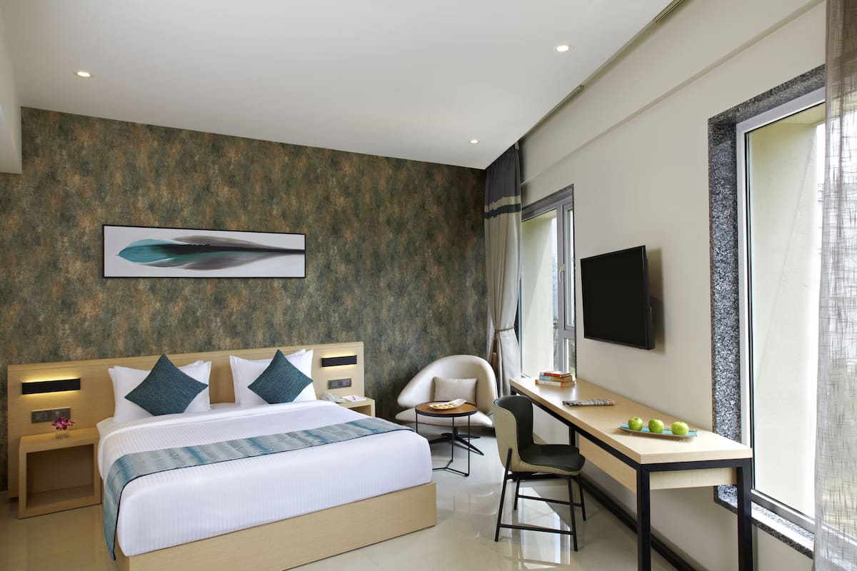 A modern hotel room with a large bed, a desk, a chair, and a TV.