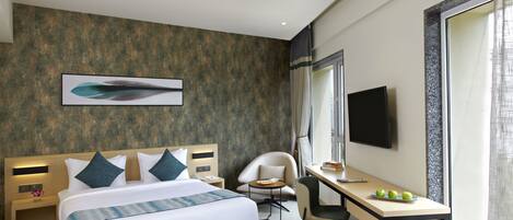 A modern hotel room with a large bed, a desk, a chair, and a TV.