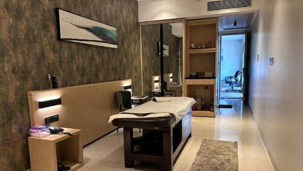 A modern hotel room with a wooden headboard, bedside table, and a massage table. There is a large mirror, a shelf with toiletries, and a door leading to another room. - Click Hotel Bangalore-International Airport (Bengaluru)