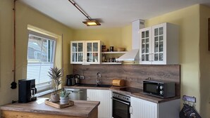 Una cocina compacta con armarios blancos, horno integrado, microondas y cafetera.