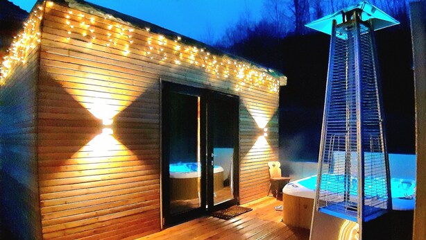 Una cabaña de madera con jacuzzi y terraza, rodeada de luces colgantes.