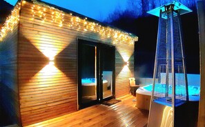 Eine Holzhütte mit Whirlpool und Terrasse, umgeben von Lichterketten.