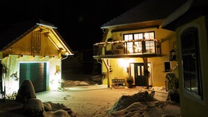 Un patio cubierto de nieve con dos casas de madera, una con balcón y chimenea, y la otra con una puerta y ventanas.