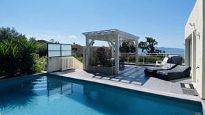 A swimming pool with a pergola and lounge chairs, surrounded by greenery and a view of the sea. - Villa with swimming pool and directly by the sea on the Rte des Sanguinaires (Ajaccio)