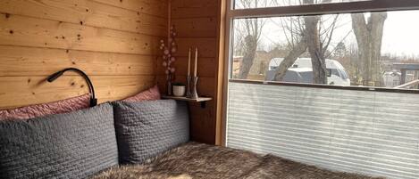 A cozy cabin room with a wooden interior, a large window, a bed with a fur rug, and a hanging light fixture.