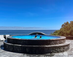 A circular infinity pool with two levels, surrounded by stone steps, overlooking a clear blue sea.