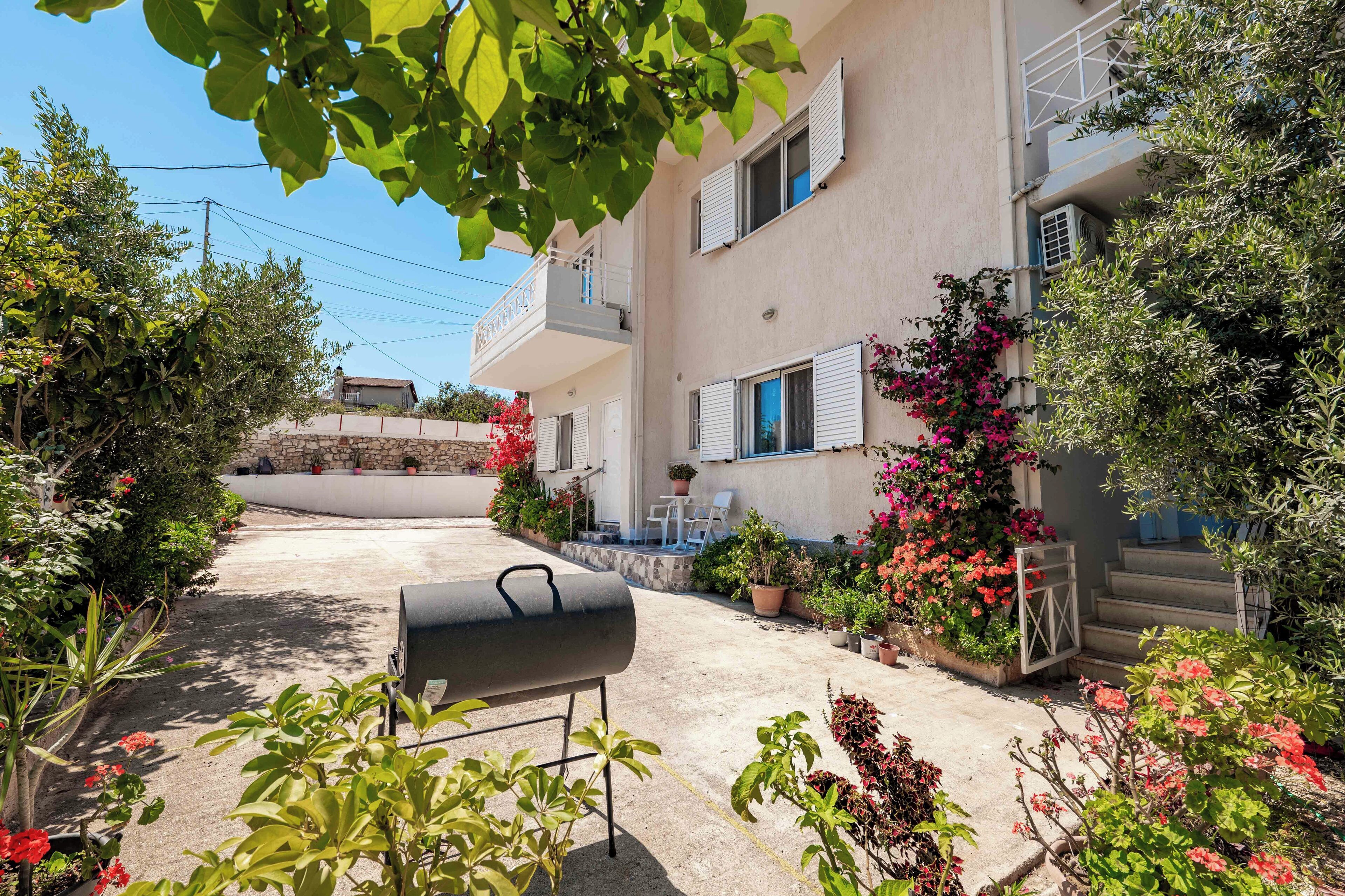 A residential building with a balcony, potted plants, and a barbecue grill in the foreground.