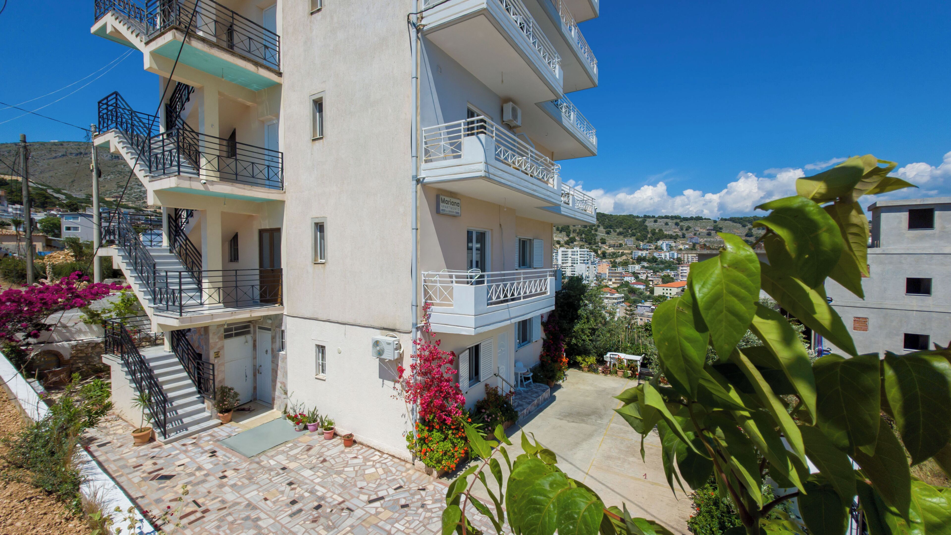 A multi-story building with balconies, a tiled patio, and surrounding greenery.
