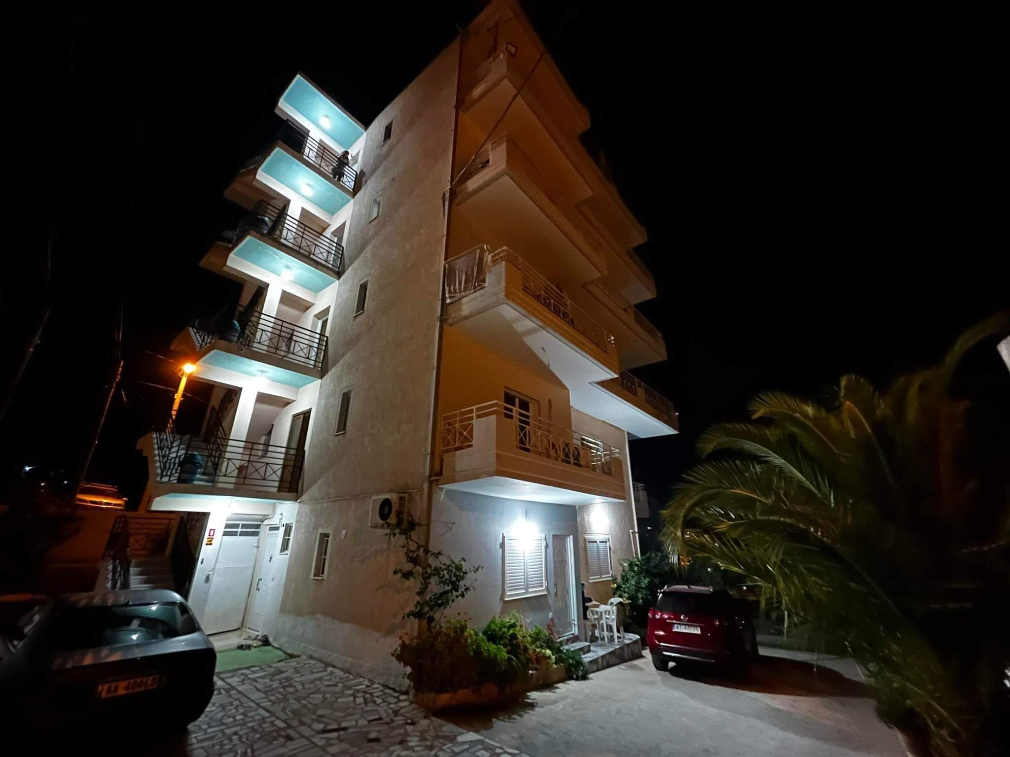 A multi-story building with balconies, a gated entrance, and a parked car.