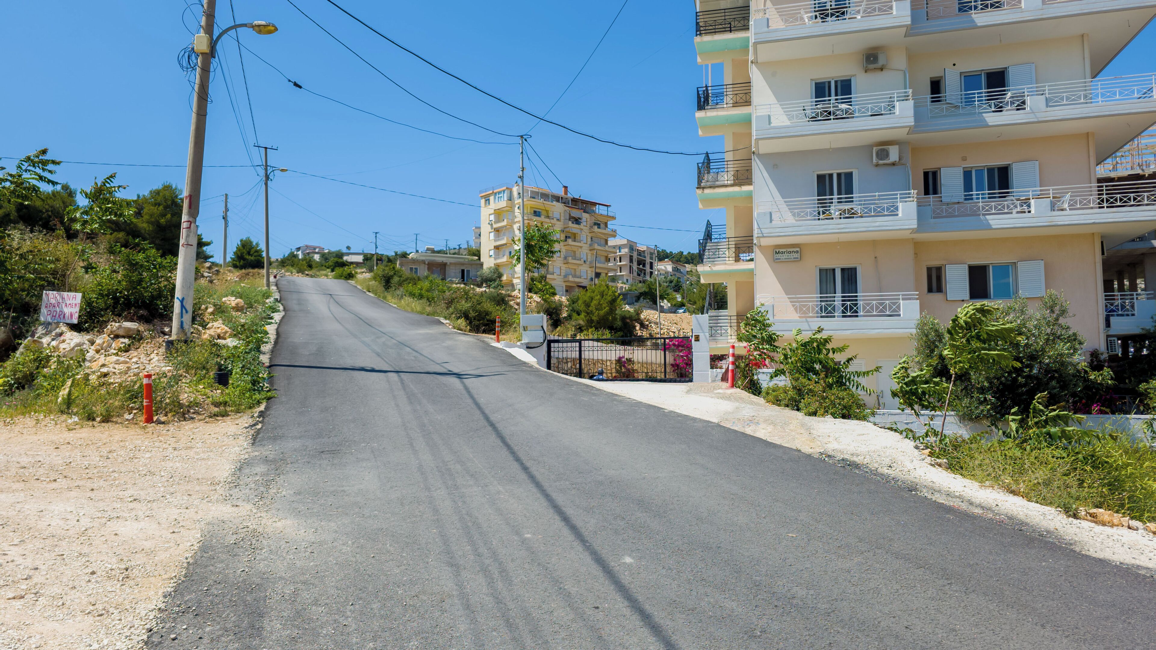 A road leading to a residential area with multi-story buildings, some with balconies.