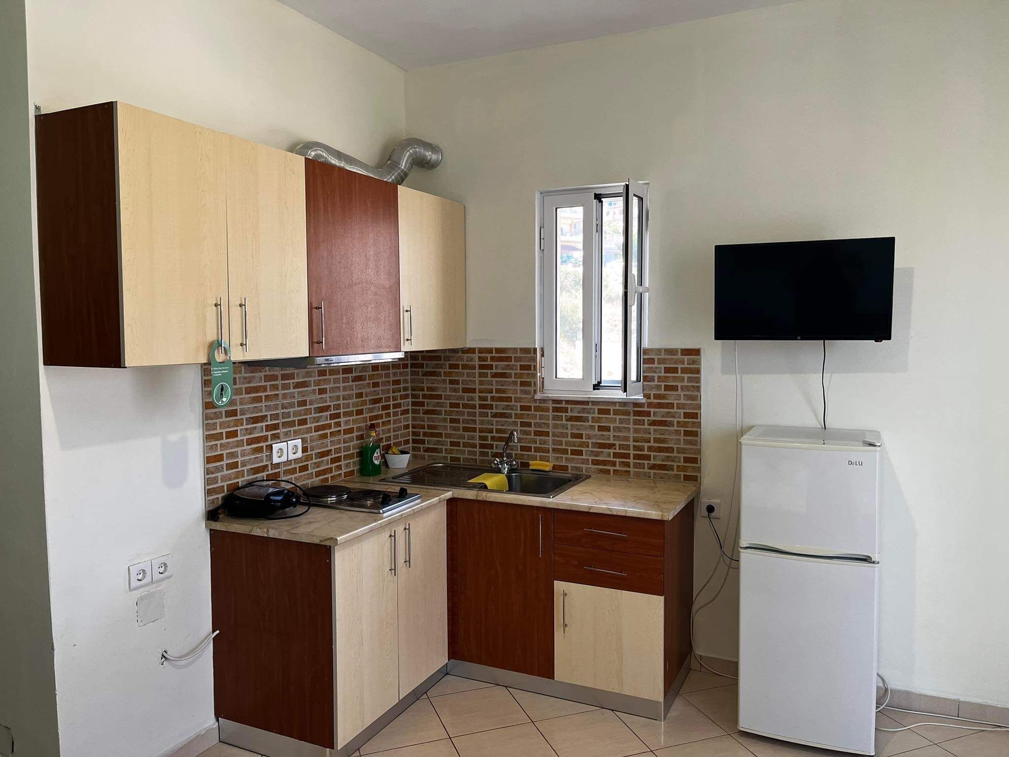 A compact kitchen with wooden cabinets, a white refrigerator, a sink, and a window.