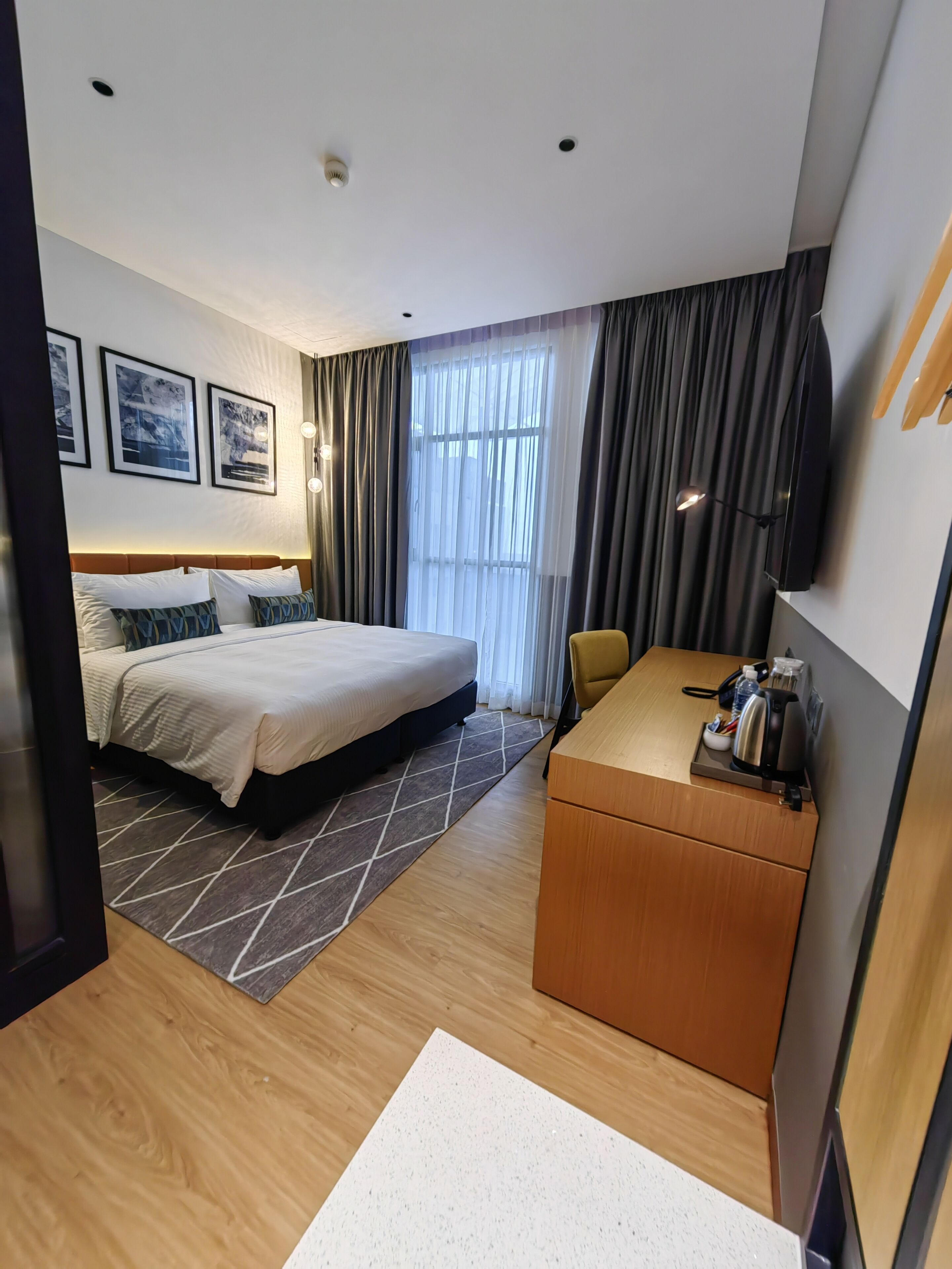 A hotel room with a bed, a desk, a chair, a TV, and a window with curtains.