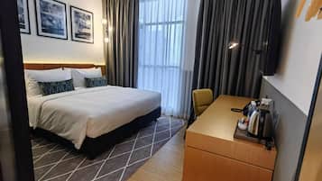 A hotel room with a bed, a desk, a chair, a TV, and a window with curtains.