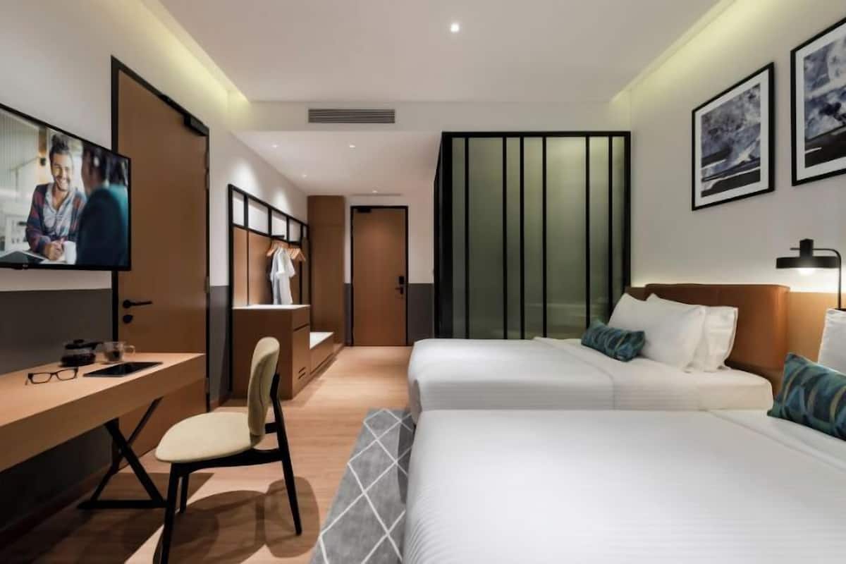 A modern hotel room with a desk, two beds, a TV, and artwork on the walls.
