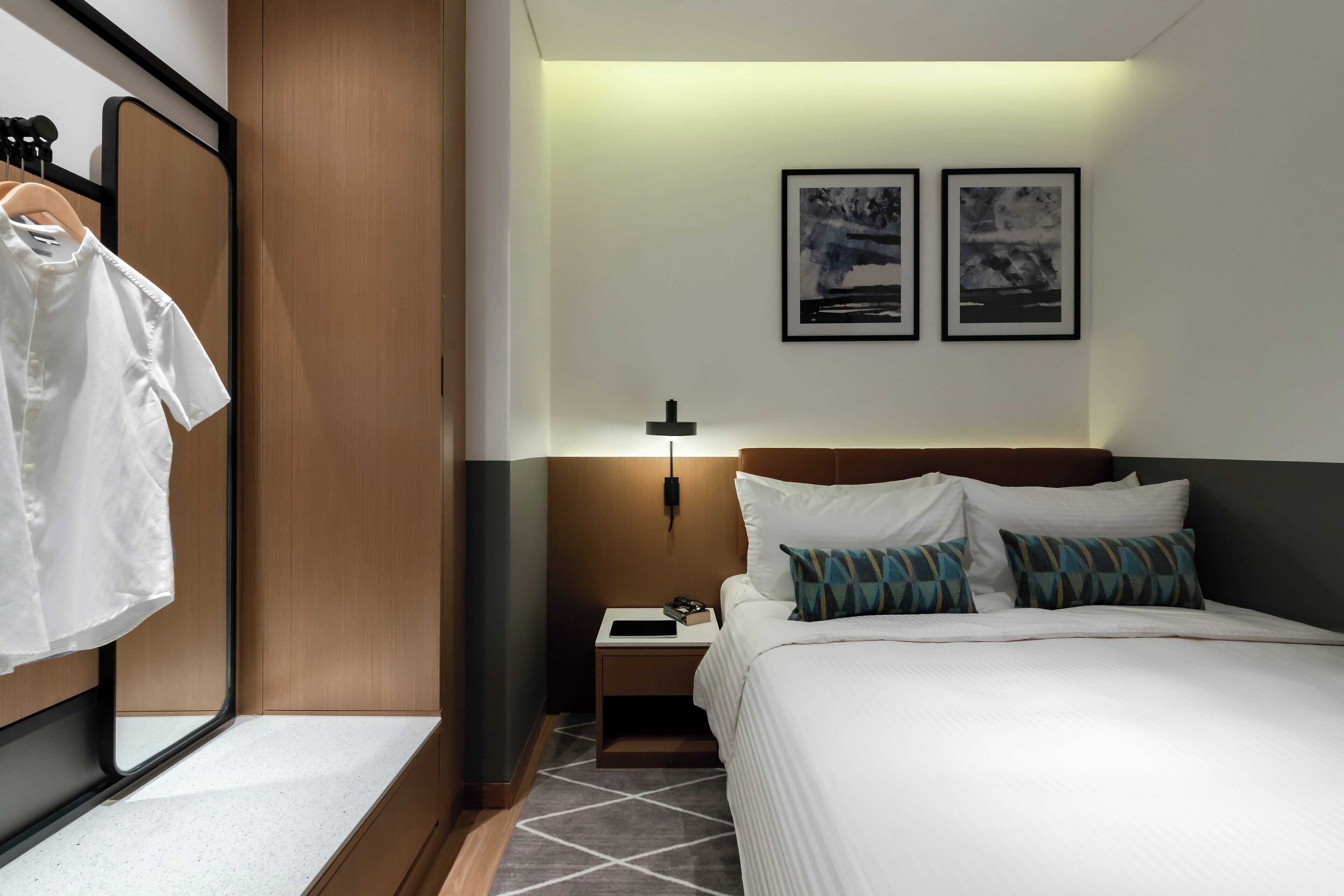 A hotel room with a bed, nightstand, and a hanging garment rack.