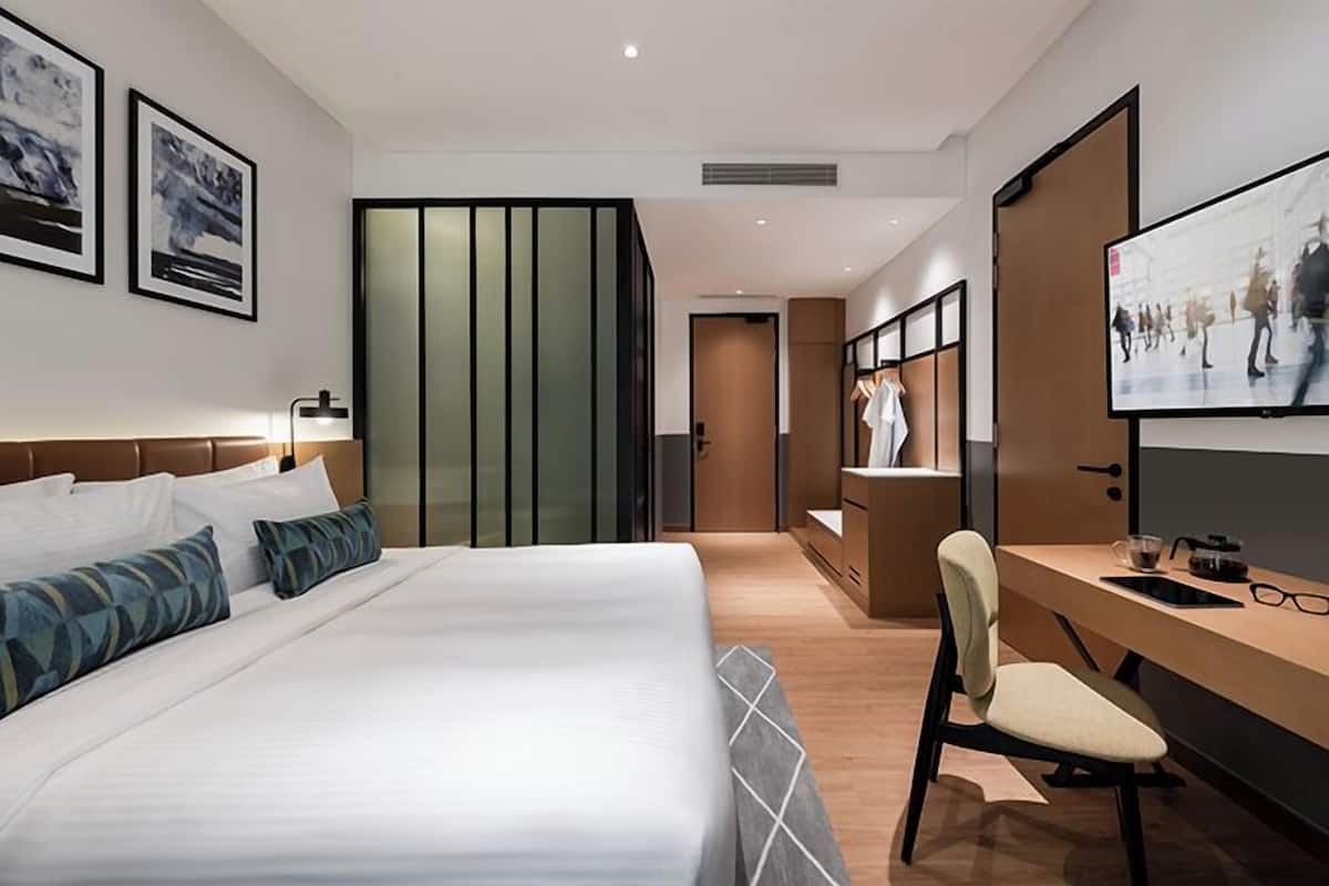 A modern hotel room with a large bed, a desk with a chair, a television, and artwork on the walls.