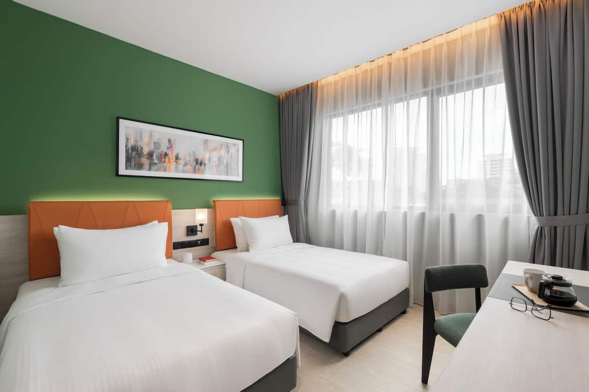 A hotel room with two beds, a desk, a chair, and a large window with curtains.