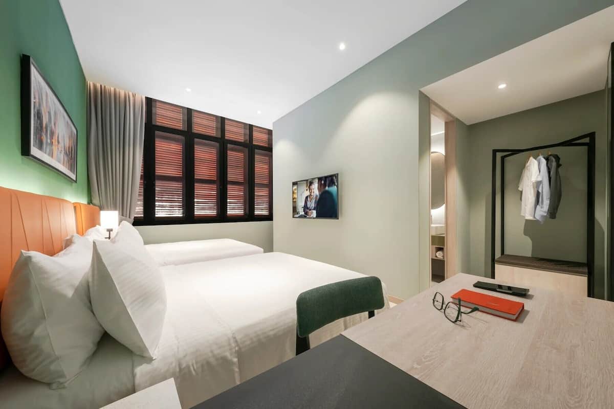 A hotel room with a bed, a desk, a chair, a mirror, and a window with blinds.