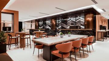 A modern kitchen with a marble island, orange chairs, and a black and white patterned backsplash.
