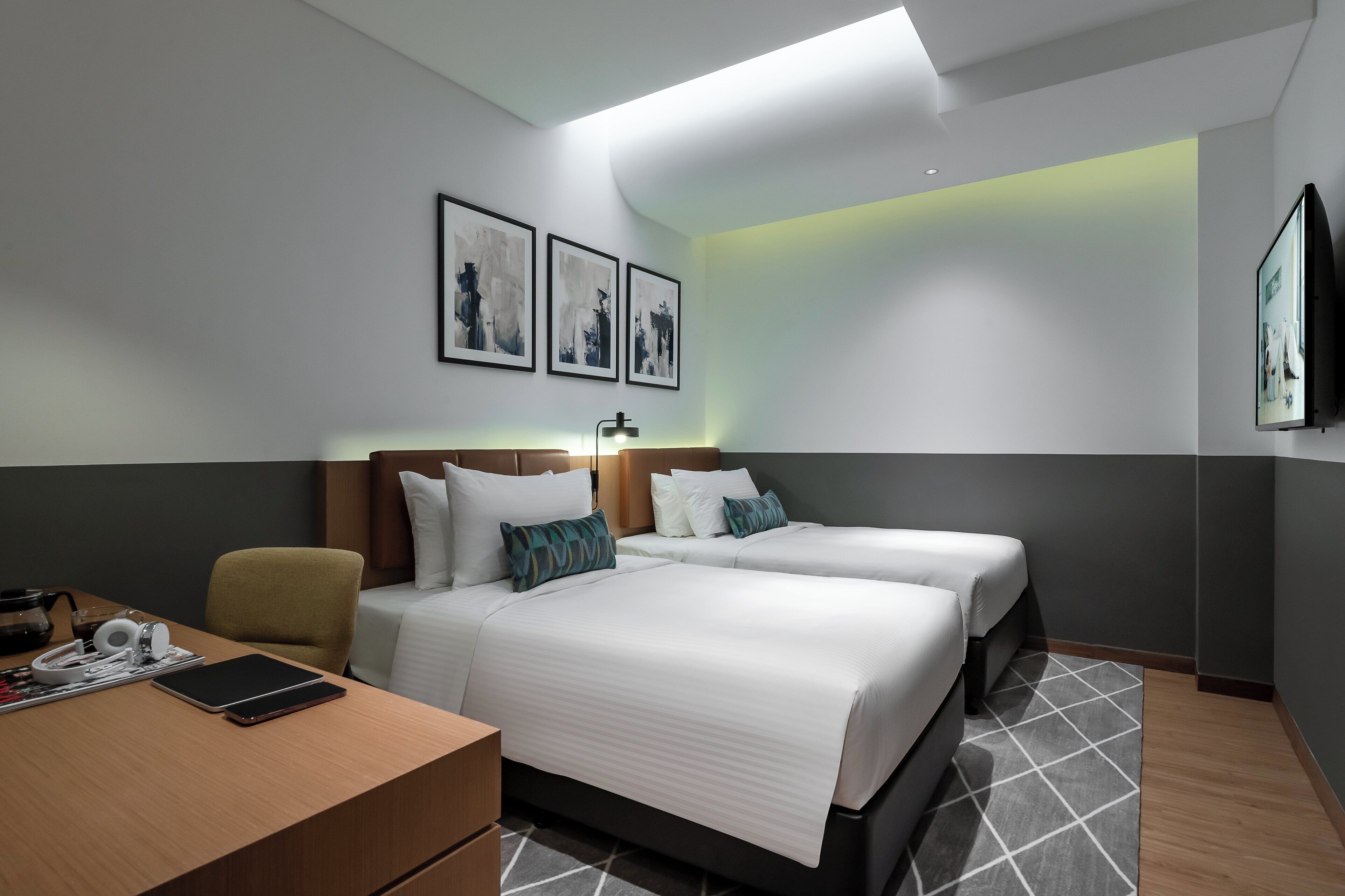 Habitación de hotel con dos camas, un escritorio con una computadora portátil, una silla y obras de arte en las paredes.