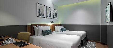Habitación de hotel con dos camas, un escritorio con una computadora portátil, una silla y obras de arte en las paredes.