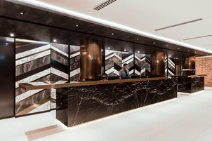 Un moderno mostrador de recepción con diseño de mármol y negro, una persona detrás y una pared de ladrillo al fondo.