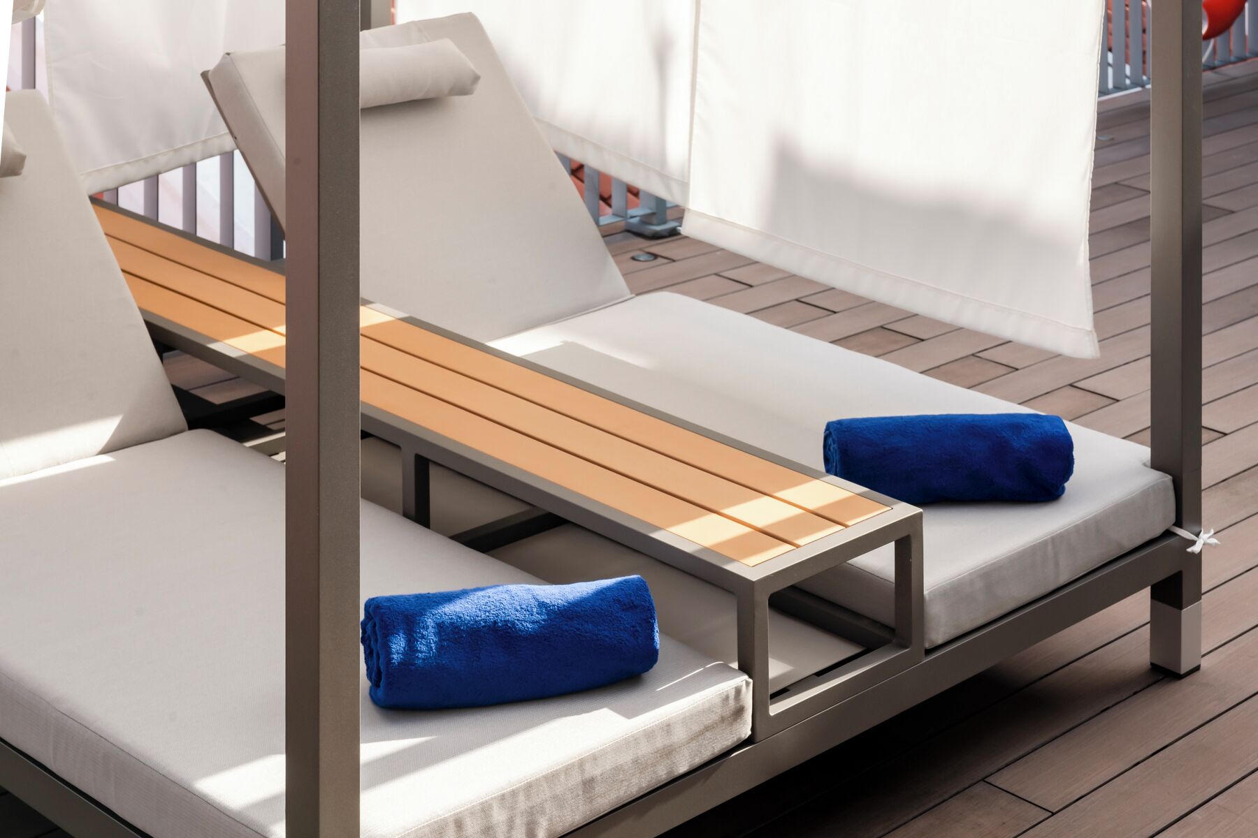 A modern outdoor lounge area with two reclining chairs, each with a wooden slat backrest and white cushions.