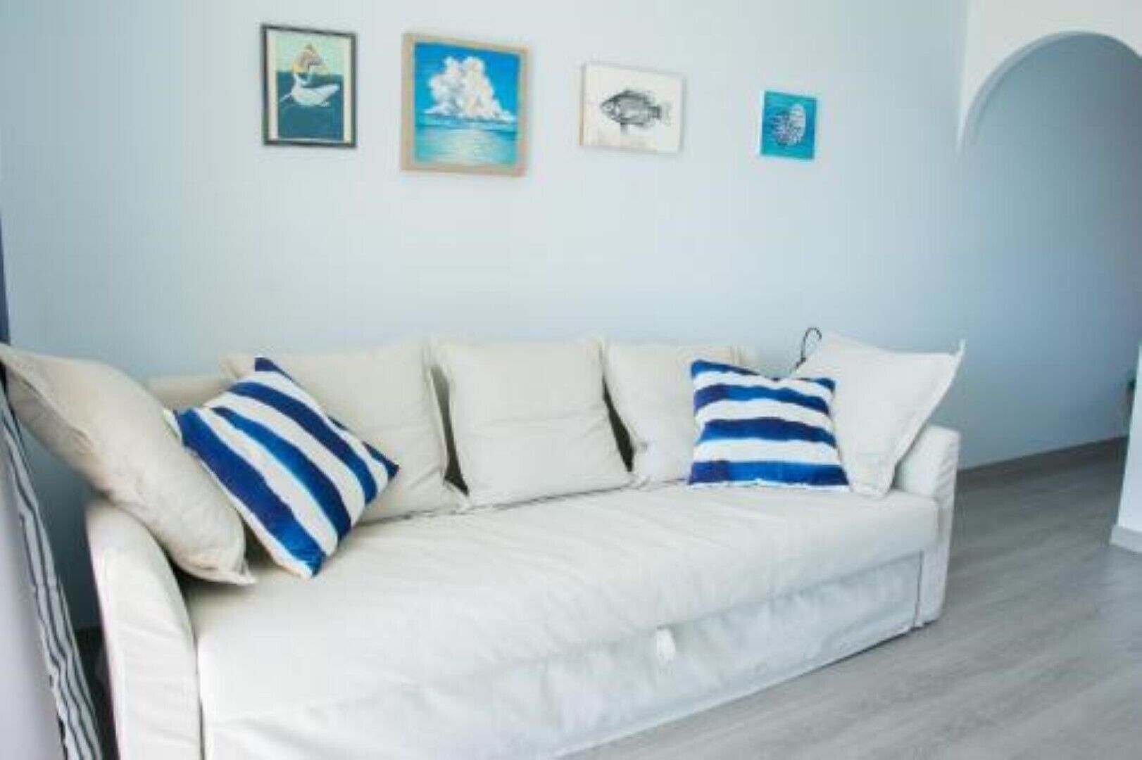 A white sofa with striped pillows against a light blue wall, accompanied by three framed artworks.