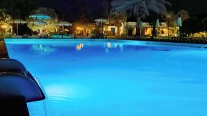 A nighttime view of a swimming pool with palm trees and outdoor seating areas. - Riva di Palo Resort (Ladispoli)