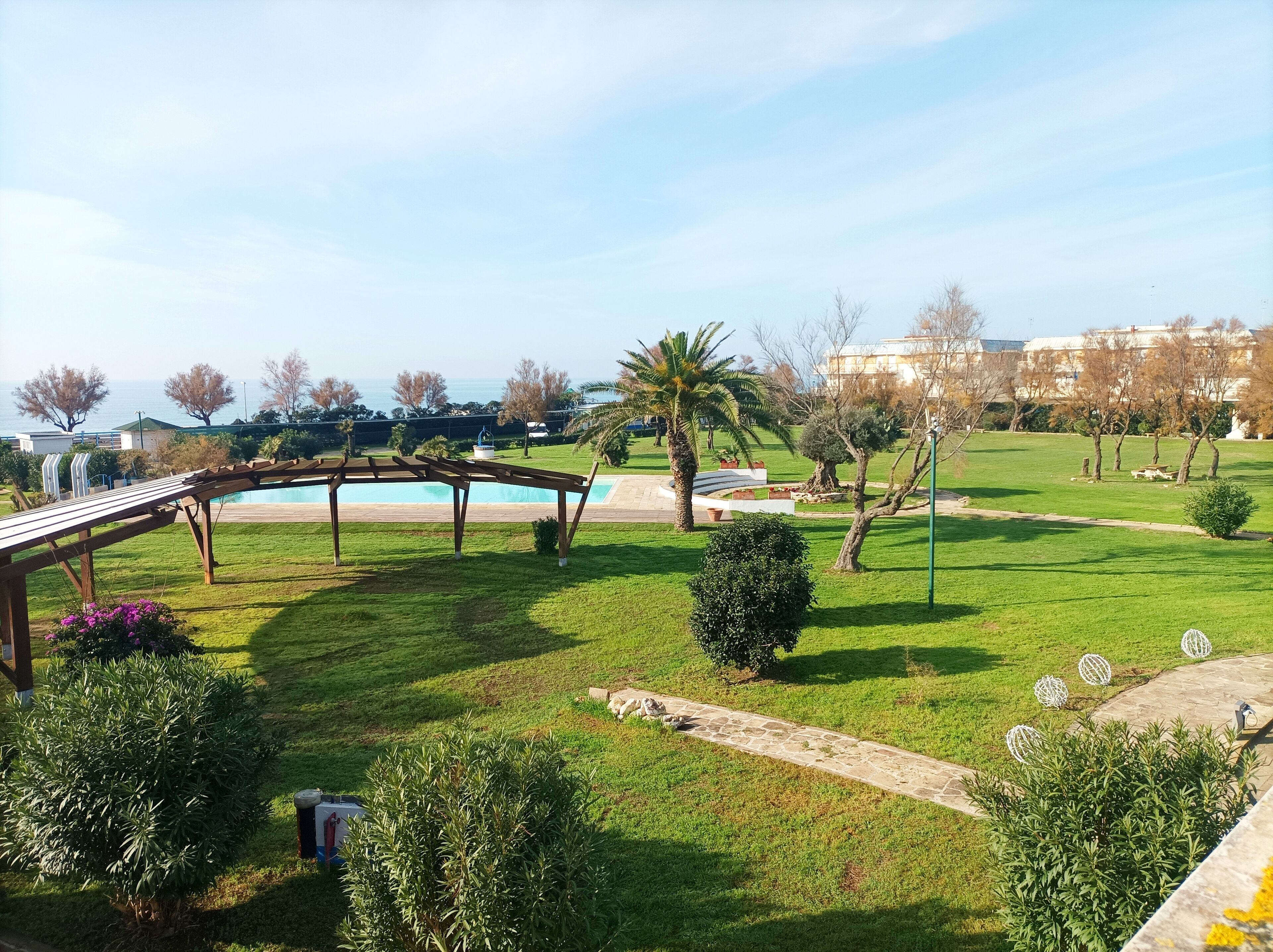 A well-maintained outdoor area with a wooden pergola, a swimming pool, and a grassy lawn with trees and shrubs.