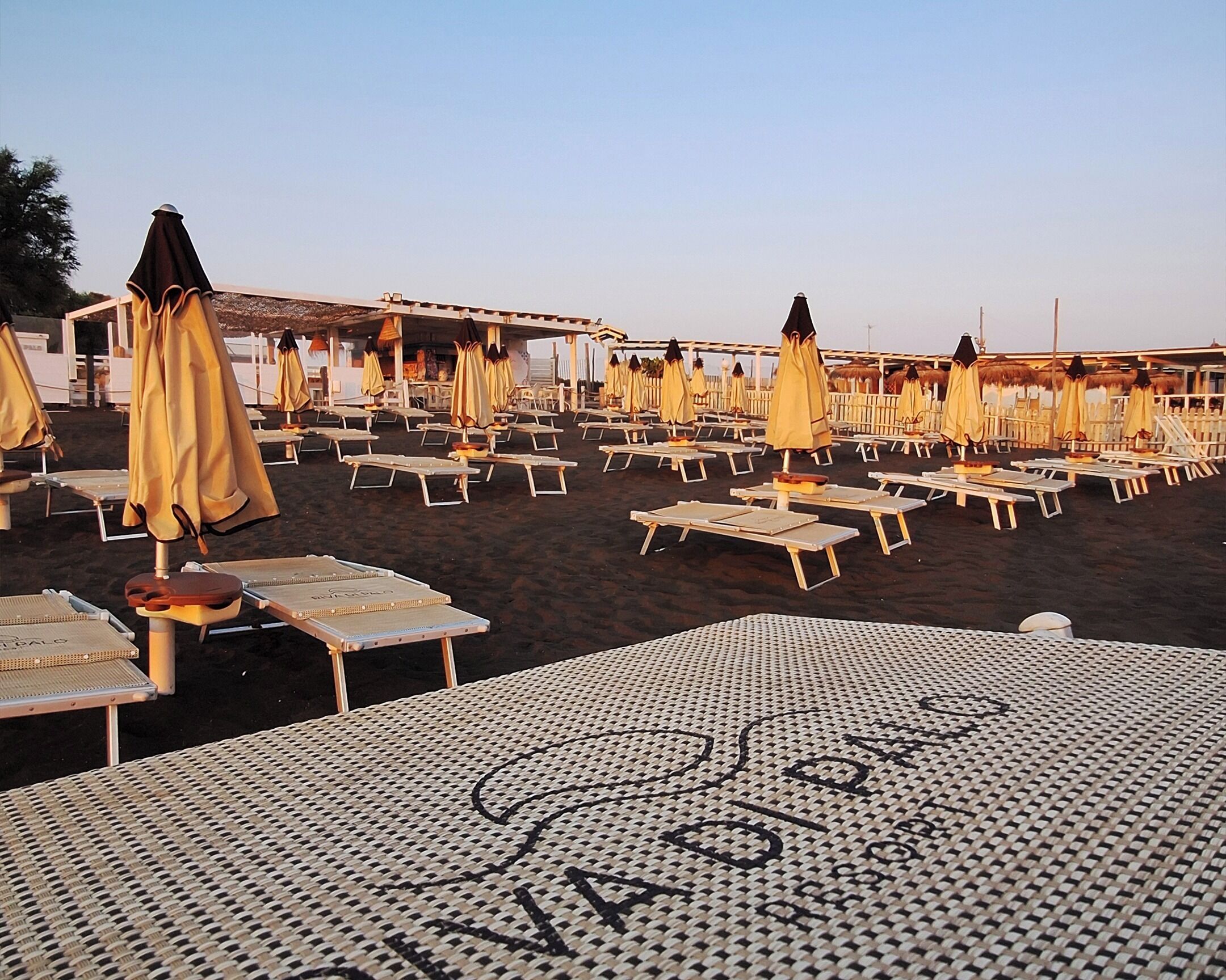Una playa con filas de tumbonas y sombrillas, una zona de estar cubierta y una mesa con motivos en primer plano.