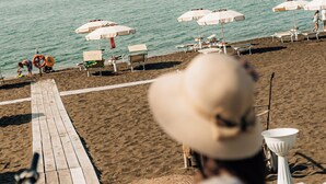 A beach scene with a wooden walkway, beach umbrellas, and lounge chairs. - Riva di Palo Resort (Ladispoli)