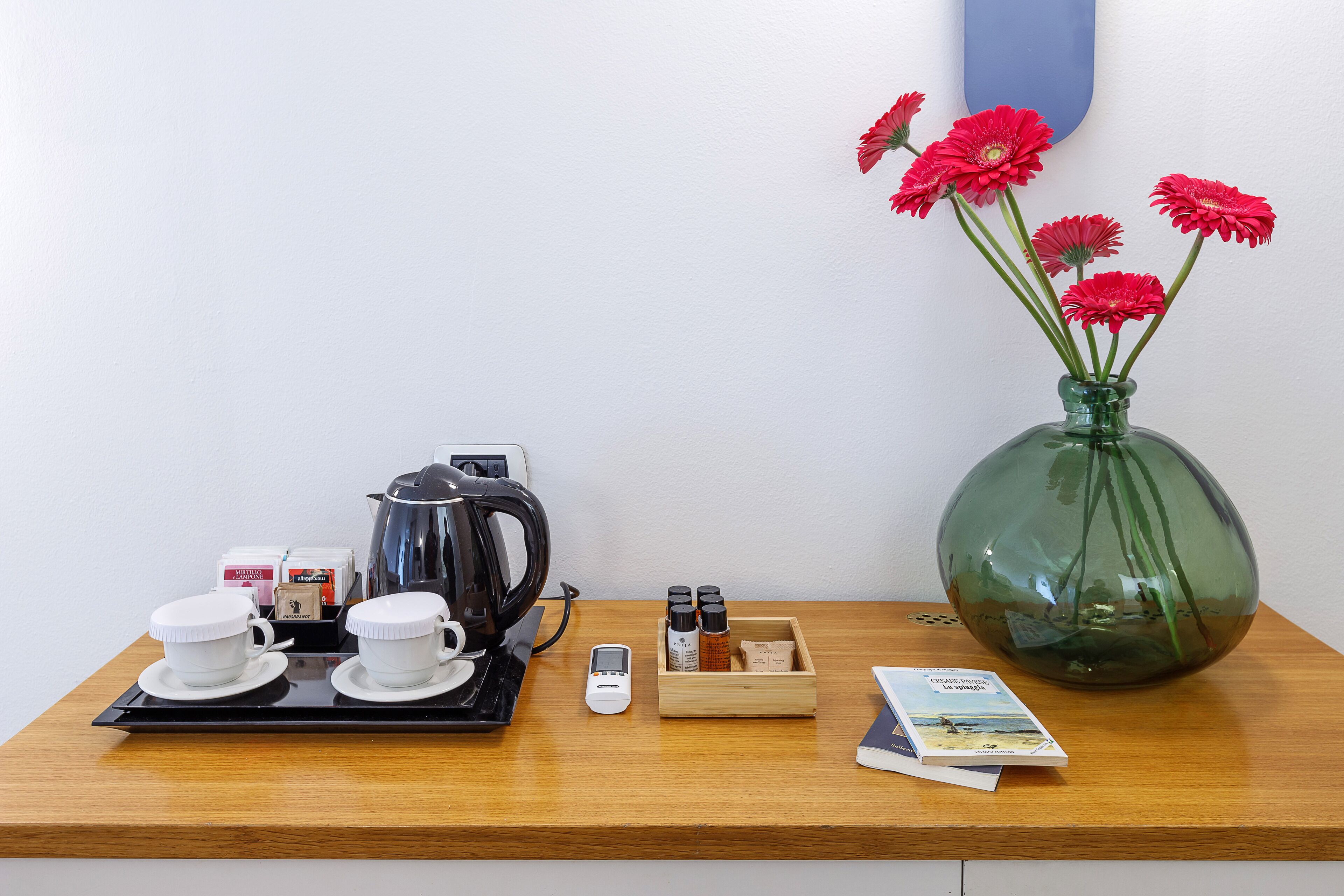 Une table en bois avec une machine à café, deux tasses, un téléphone portable, une boîte à épices, un livre et un vase avec des fleurs.