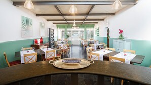 A restaurant with multiple tables and chairs, a wooden counter, and hanging pendant lights. - Riva di Palo Resort (Ladispoli)